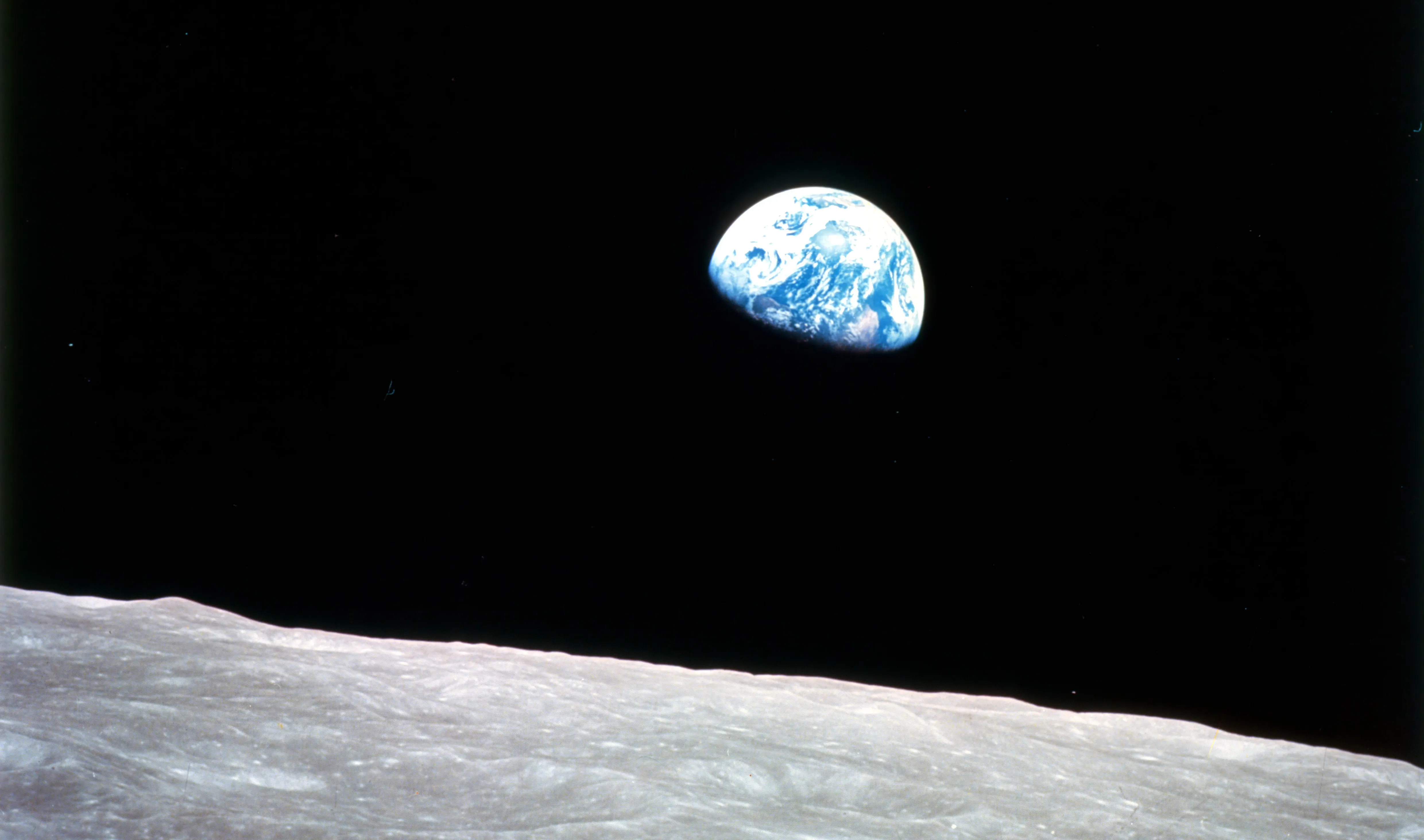 Earthrise - Apollo 8, December 24, 1968. This view of the rising Earth greeted the Apollo 8 astronauts as they came from behind the Moon after the fourth nearside orbit. The photo, by\u00a0astronaut\u00a0William Anders, is displayed here in its original orientation, though it is more commonly viewed with the lunar surface at the bottom of the photo. Earth is about five degrees left of the horizon in the photo. The unnamed surface features on the left are near the eastern limb of the Moon as viewed from Earth. The lunar horizon is approximately 780 kilometers from the spacecraft. Height of the photographed area at the lunar horizon is about 175 kilometers.